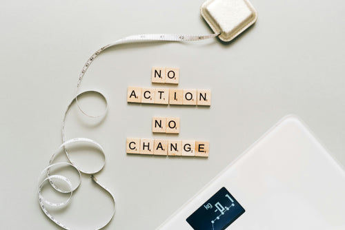 Measuring tape with 'No Action No Change' on wooden blocks, digital scale in the corner.