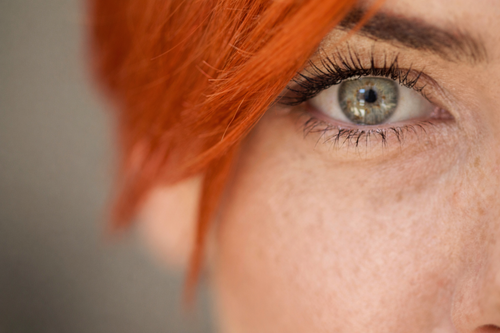 Close-up of a person with orange hair and blue eyes against a neutral background